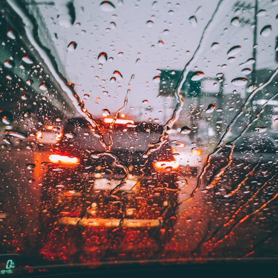 Blurred city traffic seen through a rain-soaked windshield, capturing the moody atmosphere of a wet day.